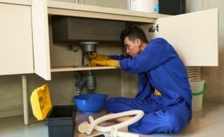 Plumber working on a sink drain under a cabinet, representing commercial plumbing in Parker, CO.